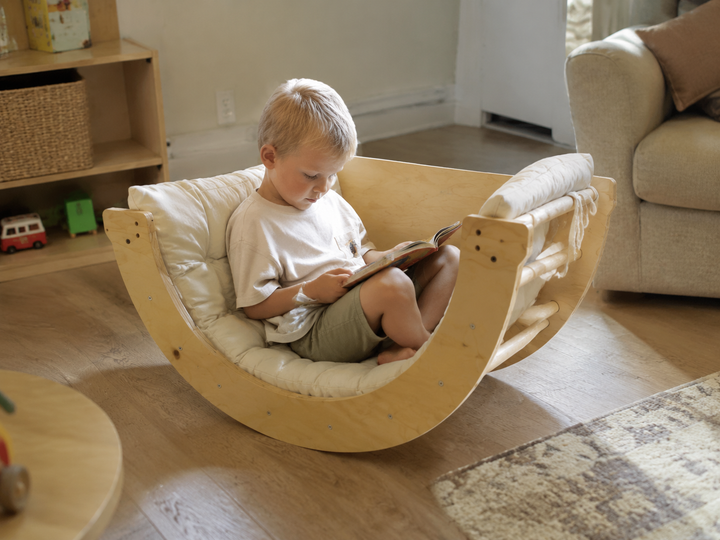 Child reading a book in a Montessori wooden rocker chair at home