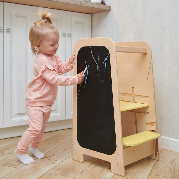 Child using a wooden kitchen helper tower during a family activity